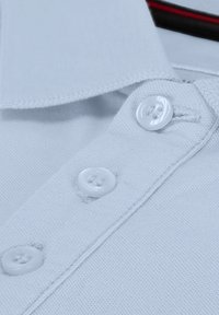 Lichtblauw polo-shirt met een klassieke kraag, drie witte knopen en een gestructureerde stof. Gestikte accenten zichtbaar langs de kraag.