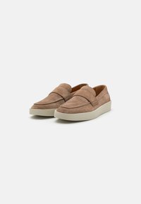 Pruunist nahast slip-on jalanõud, millel on minimaalne disain, lame kummitald ja üleval õmmeldud detailid.