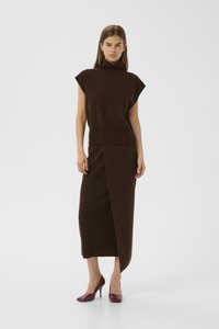 Brown knit top with a high collar and short sleeves, paired with a fitted brown ankle-length skirt featuring a side slit. Worn with burgundy heels.