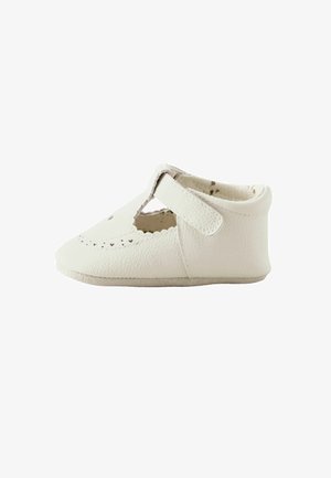 Scarpina bianca per bambini con cinturino a T e piccoli ritagli a forma di cuore sul davanti, realizzata in materiale morbido e strutturato.