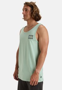 Mintgrünes Tanktop aus weichem Stoff, mit einer quadratischen Tasche, die ein Wellenmotiv und einen kontrastierenden Rand aufweist. Runder Halsausschnitt, ärmelloses Design.