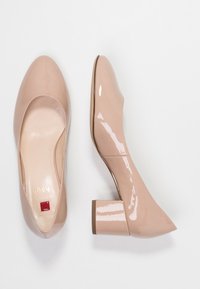 Nude lackläder skor med blockklack och rund tå, med en slät yta och en liten röd accent på innersulan.
