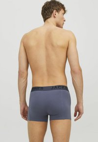 Bóxer gris para hombre con una cinturilla elástica negra que presenta el logo "JACK & JONES". Material suave, diseño ajustado y longitud de pierna corta.