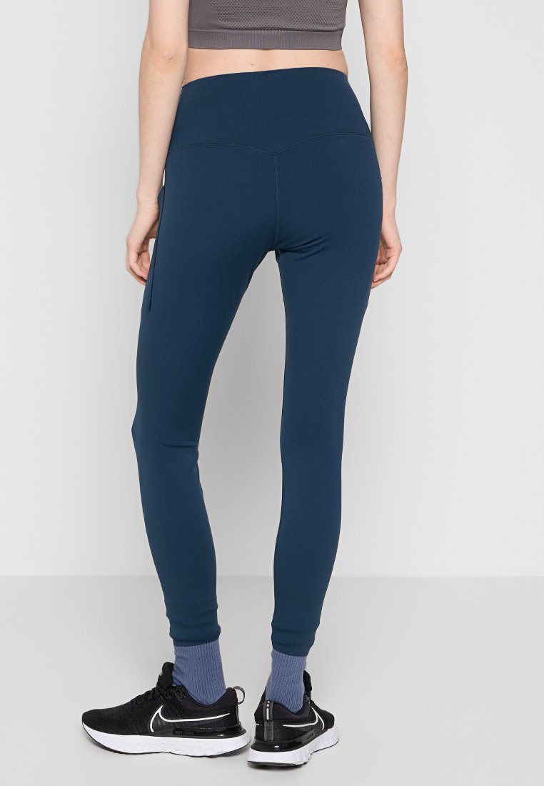 Leggings azul marino hechos de material elástico, con cintura alta, diseño elegante y corte hasta el tobillo, combinados con zapatillas de correr negras.