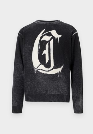 Czarny sweter z okrągłym dekoltem z dużą białą literą "G" w stylu gotyckim na plecach, z efektem kapania farby.