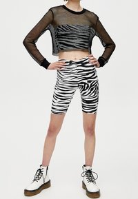 Zwarte mesh cropped longsleeve top over witte en zwarte zebra print fietsbroek, gecombineerd met witte combat boots met dikke zolen.