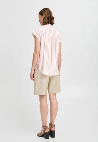 Camisa de manga corta a rayas en color rosa claro y blanco, con aberturas laterales y un corte relajado, combinada con pantalones cortos beige y sandalias de tacón.