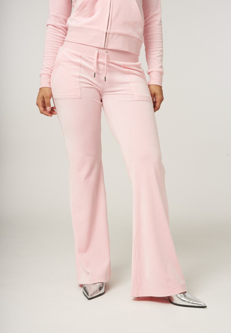 Lichtroze, uitlopende sweatpants van zachte stof met een tailleband met trekkoord en voorzakken. Gecombineerd met zilveren, puntige hakken.