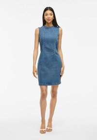 Robe sans manches en denim avec un col haut, une forme cintrée et des détails de couture visibles. La couleur est bleu moyen avec un ourlet. 