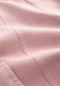 Lichtroze linnen stof met een fijne weving en subtiele textuur. Bevat gestikte naden, wat de zachtheid en een gladde oppervlakte laat zien.