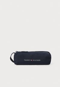Marinblå pennskrin tillverkat av hållbart tyg, med dragkedjestängning, handtag och vit "TOMMY HILFIGER"-logotyp tryckt på framsidan.