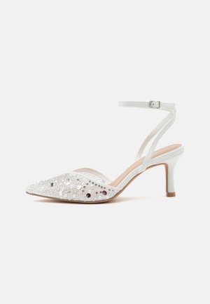 Zapato blanco de tacón medio con tira en el tobillo, puntera puntiaguda decorada con lentejuelas y cuentas, mostrado de perfil sobre fondo liso.