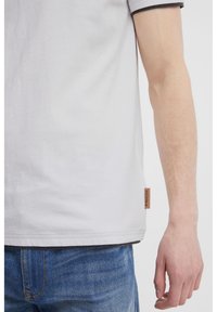Light gray t-shirt made of cotton, featuring dark gray trim on the collar, and a small brown fabric label on the lower side.