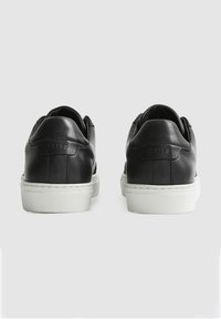 Sneakers in pelle nera con suola in gomma bianca, finitura liscia, design minimalista e logo 'REISS' in rilievo discreto sul tallone.