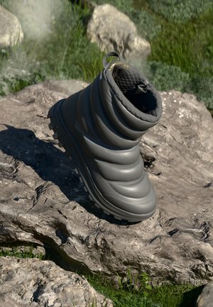 Botte de plein air grise, rembourrée et moelleuse, avec une tige texturée, une semelle en caoutchouc et une languette. Posée sur une roche avec de l'herbe en arrière-plan.