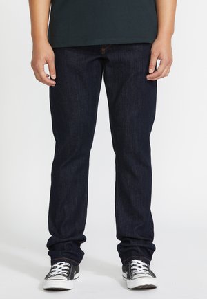 Donkerblauwe denim jeans met een rechte pijpontwerp, voorzien van zichtbare stiksels, gecombineerd met zwart-witte sneakers.