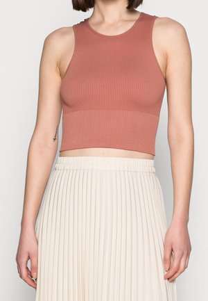 Woman wearing a sleeveless, ribbed, dusty rose crop top paired with a high-waisted, cream-colored pleated skirt.