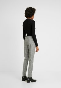 Black long-sleeve top and gray checked trousers. Trousers feature a fitted design and side pockets. Model wears black heeled ankle boots.