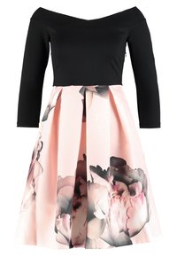 Svart topp med avskuret axelparti och trekvartsärmar, kombinerad med en ljusrosa kjol med blommönster och plisserad design.