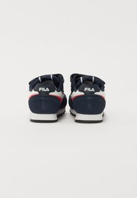 Tummansinisiä lenkkareita, joissa on valkoisia ja punaisia yksityiskohtia, joissa on teksturoidusta kankaasta valmistettu päällinen, kestävä pohja ja Fila-logot kantapäässä.