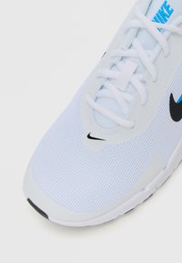 Nahaufnahme eines weißen Nike-Laufschuhs, der das Mesh-Gewebe, die Schnürsenkel, das blaue Nike-Logo auf der Zunge und den schwarzen Nike-Swoosh an der Seite und der Zehe zeigt.