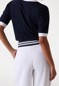 Navy cropped top with white collar and sleeves, paired with high-waisted white pants featuring a black and white striped waistband.