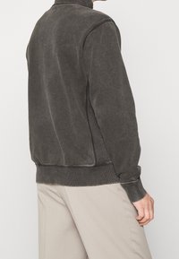 Mörkgrå sweatshirt med en texturerad yta, ribbade ärmslut och nederkant, samt hög krage. Baksidan är enkel med diskreta sömmar.