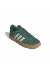 Zielony sneaker Adidas z białymi paskami i gumową podeszwą, zasznurowany, ustawiony skośnie w lewo na białym tle.