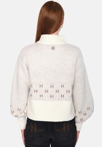 Kremfarget genser med høy krage, strukturert stoff, ballongsleeves og brun gjentatt 'H'-mønster langs kantlinjen.