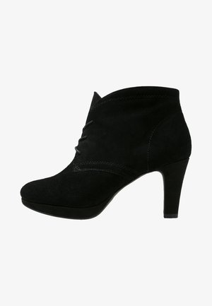 Mustat samettiset nilkkurit, joissa on terävä kärki, kaareva yläreuna ja 10 cm korkeat kantapää. Edessä on koristeellista ommeltua yksityiskohtaa.