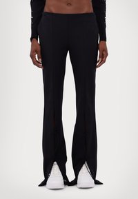 Calças largas pretas com fendas na parte de baixo, apresenta detalhes com laços. Feitas de um tecido suave. Combinadas com ténis brancos.