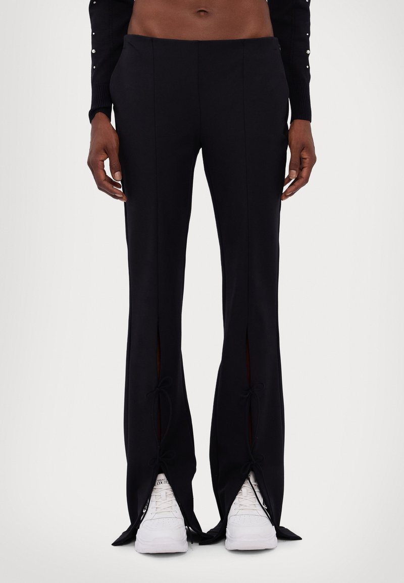 Calças largas pretas com fendas na parte de baixo, apresenta detalhes com laços. Feitas de um tecido suave. Combinadas com ténis brancos.