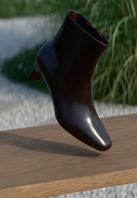 Shiny black leather ankle boot with a low heel displayed above a wooden surface with green plants in the background.