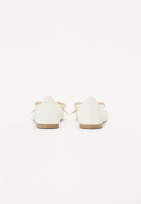 Ballerines blanches en cuir lisse, avec un petit talon, un bout rond et deux nœuds décoratifs à l'arrière.