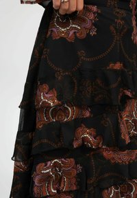 Robe noire à volants avec des motifs floraux marron et violet, fabriquée en tissu léger. Détails comprenant des volants superposés et des designs complexes.