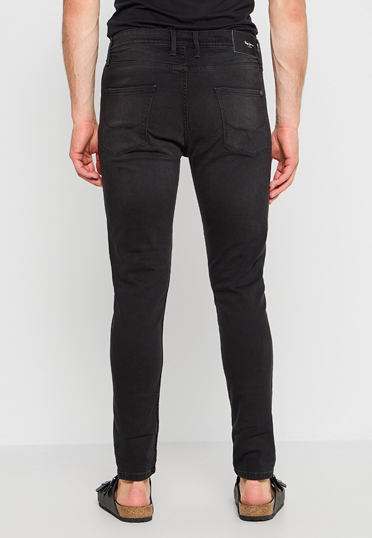 Jeans negros de corte ajustado con una textura suave, que presentan dos bolsillos traseros y una etiqueta de marca en la cinturilla. Llevados con sandalias de punta abierta.