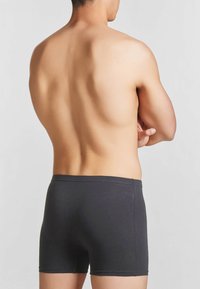 Boxer shorts neri in cotone, vestibilità aderente, texture liscia, senza motivi visibili, design semplice, con vita elastica. Vista posteriore di una persona.