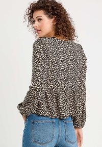 Blouse en imprimé léopard en tissu léger, manches longues, ourlet plissé, encolure ronde, avec un fond beige et des taches noires.