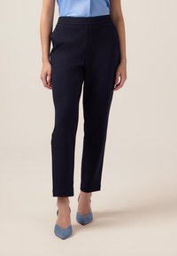 Pantalones navy con una tela suave, diseño ajustado, bolsillos laterales y una cintura elástica, combinados con tacones puntiagudos de color azul claro.