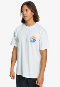 White cotton t-shirt featuring a circular graphic with a wave and mountain design in red, orange, blue, and yellow. Standard fit, short sleeves.