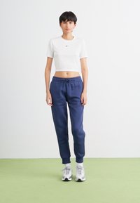 Hvit cropped t-skjorte med svart logo, sammen med marineblå joggebukser med elastisk midjebånd og mansjetter, brukt med grå treningssko.