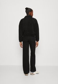Sort, struktureret fleece-pullover med høj krave og sidelommer, parret med sorte bukser med lige ben og sneakers med hvide detaljer.