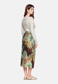 Beige Langarmoberteil kombiniert mit einem knielangen Rock mit floralem Muster in den Farben Grün, Orange und Braun; Model trägt beiger Ballerinas.