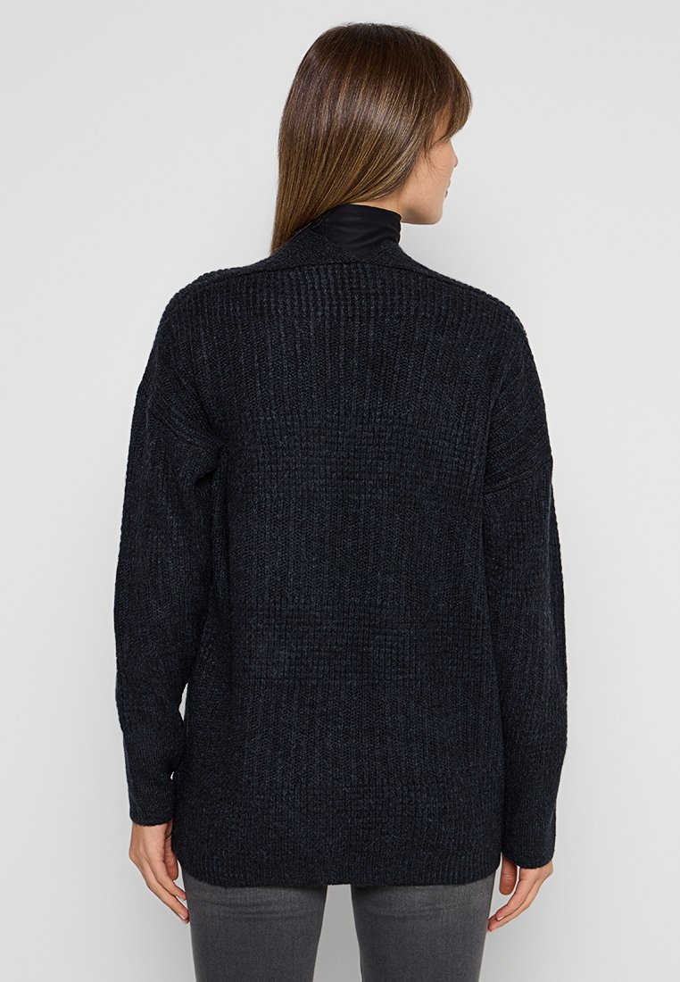 Ciemnoszary, oversize dzianinowy sweter z teksturowanym wzorem, z opadłymi ramionami i wysokim kołnierzem. Ściśnięte mankiety i dół. Minimalistyczny design.