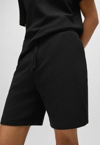 Shorts tissés noirs avec un motif texturé, dotés d'une taille élastique avec cordon de serrage et d'un discret logo sur l'ourlet.