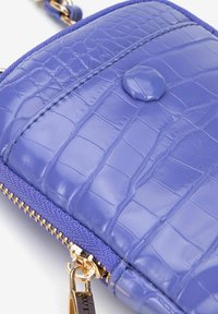 Portafoglio viola con texture coccodrillo, dotato di hardware in oro per la zip e chiusura a pulsante rotondo. Finitura liscia con profili in tessuto contrastante.