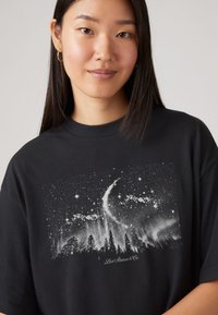 Sort bomulds-T-shirt med et hvidt grafisk tryk af en stjerneklar nattehimmel med træer og teksten "Levi Strauss & Co." nederst.