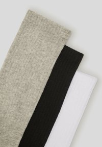 Trzy pary skarpet z prążkowanego materiału: jasnoszare, czarne i białe. Każda skarpeta charakteryzuje się miękką fakturą i równą, jednolitą grubością.