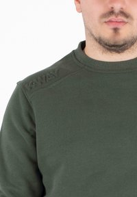 Donkergroene sweatshirt met ronde halslijn en textuurdetail op de schouders, voorzien van het "K-WAY"-logo in geborduurde letters.