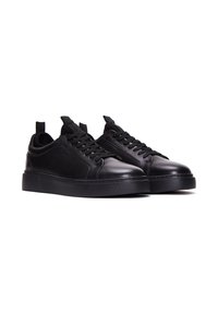 Un paio di sneakers in pelle nere a basse, con lacci neri e suole in gomma spessa, mostrati affianco su uno sfondo bianco.